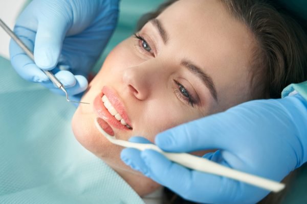 Close up of stomatologist hands in sterile gloves checking female teeth with dental mirror and explorer while woman lying in dental chair