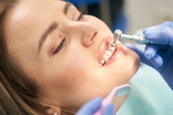 Close up of dentist in sterile gloves cleaning and polishing female teeth with dental polisher device